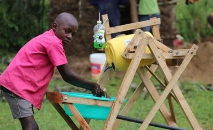 Stephen Wamukota, um queniano de 9 anos, com a máquina que ele criou para lavar as mãos e evitar infecção pelo coronavírus. Foto - redes sociais
