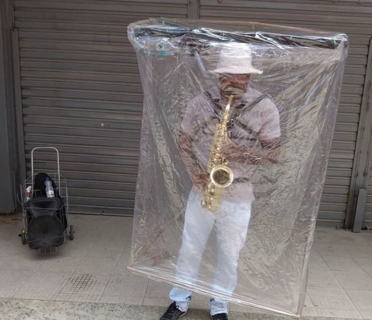 Músico toca saxofone protegido por cabine de plástico